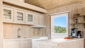 Una cocina con armarios de madera, lavavajillas integrado, cafetera y ventana con vista a zonas verdes.