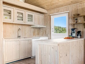 Eine Küche mit Holzausstattung, einem integrierten Geschirrspüler, einer Kaffeemaschine und einem Fenster mit Blick auf Grünflächen.