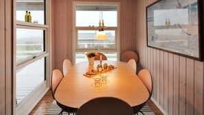 Un comedor con una mesa de madera, sillas, una lámpara colgante y un ventanal con botellas en el alféizar.