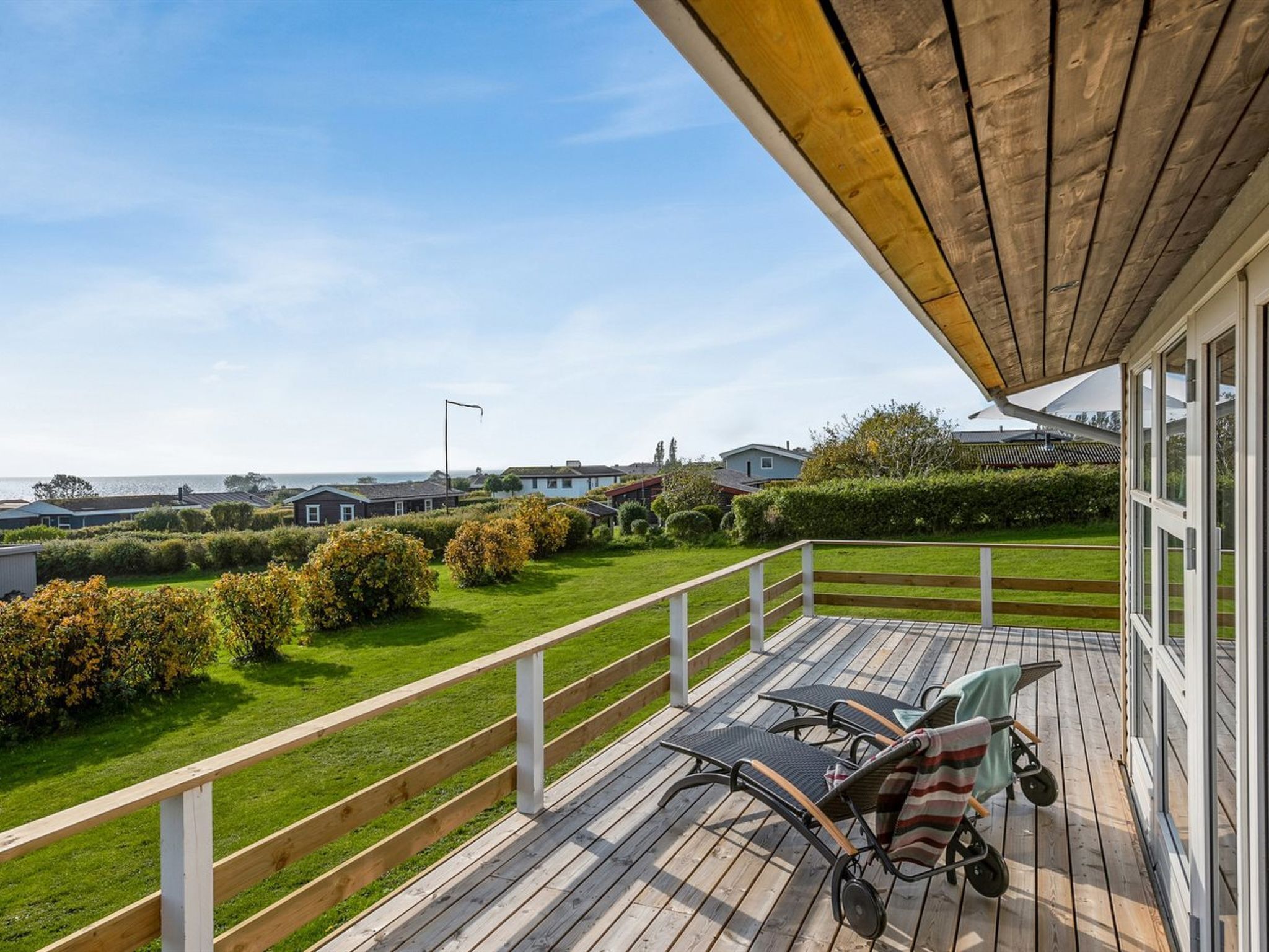 A wooden deck with outdoor furniture, a view of a grassy area, and a body of water in the distance.