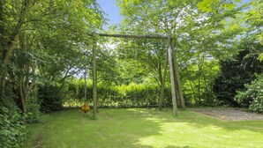 A grassy outdoor area with a swing set and dense foliage. - "Claudia" by Interhome (Bredebro)