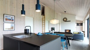 Una cocina moderna con una isla central, un comedor con sillas azules, una chimenea y una sala de estar con sofá y televisor.