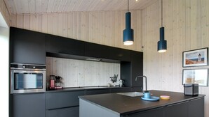Una cocina moderna con una isla central, horno empotrado e iluminación colgante.