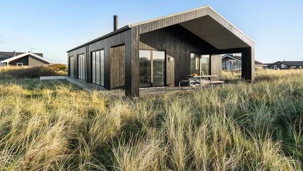 Una casa moderna con un amplio patio abierto, rodeada de hierba alta.