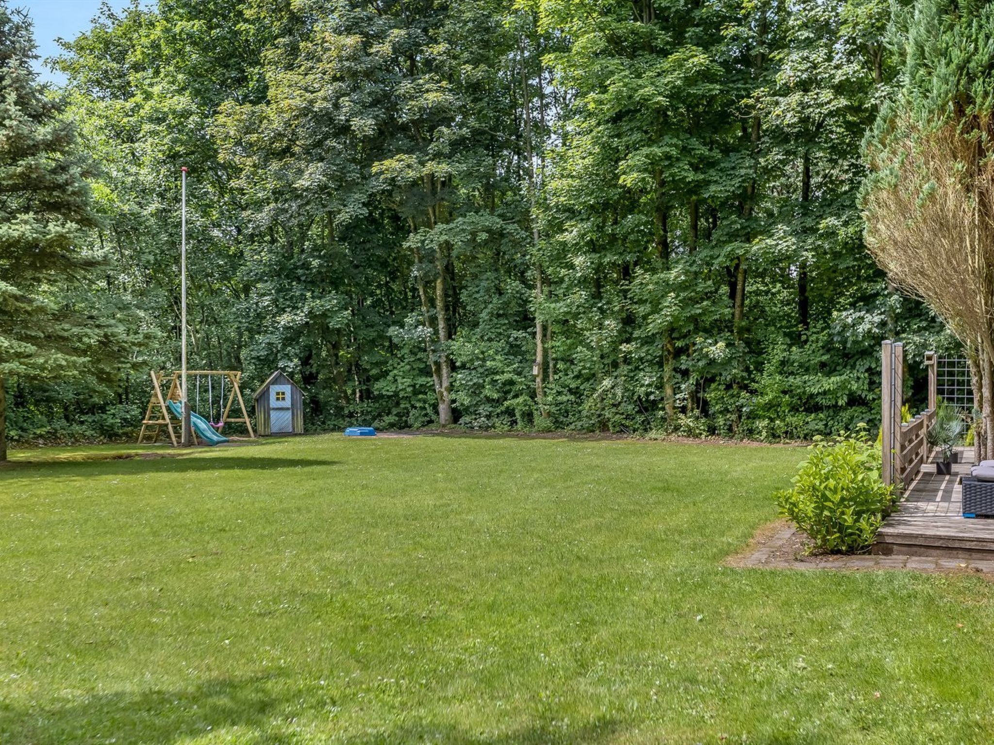 A grassy backyard with a wooden swing set and a small shed.