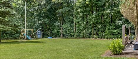 A grassy backyard with a wooden swing set and a small shed.
