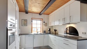 Une cuisine moderne avec des meubles blancs, un four encastré, une machine à café et une hotte noire.