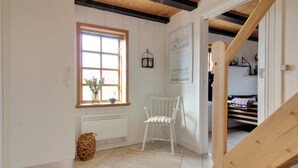Une pièce avec une chaise blanche, une fenêtre donnant sur un paysage, un radiateur et un escalier en bois.