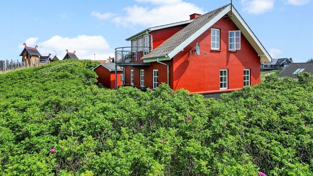 Une maison rouge avec un balcon, entourée d’une végétation verdoyante.