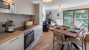Eine moderne Küche mit eingebauter Mikrowelle, Toaster und Backofen. Ein Essbereich mit Holztisch und Stühlen lädt zum Verweilen ein, und ein großes Fenster bietet einen Blick ins Freie.