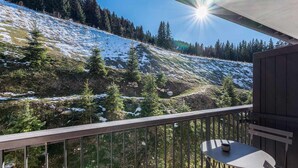 Ein Balkon mit Tisch und Stühlen, der Blick auf einen schneebedeckten Hang mit Bäumen gewährt.