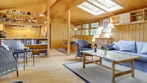 Et rummeligt træinteriør med høje lofter, ovenlys og forskellige siddeområder, herunder en sofa og stole.