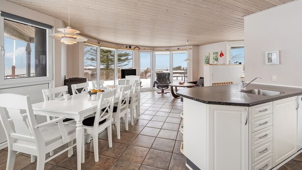 Una cocina moderna con armarios blancos, una isla grande y una zona de comedor con sillas blancas.