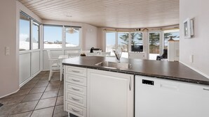 Una cocina moderna con armarios blancos, encimera negra y un amplio ventanal con vistas a un paisaje nevado.