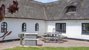 A courtyard with a thatched roof building, a stone bench, and a table with a bottle and glass.