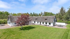 A traditional thatched-roof building with a white exterior, multiple windows, and a small garden area with a bench and a tree.