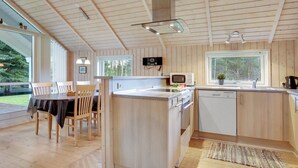 A modern kitchen with wooden paneling, a central island, a dining area with a table and chairs, and large windows providing natural light. - "Lisel" - 25km from the sea by Interhome (Toftlund)