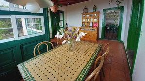 Un coin repas avec une table carrelée, des chaises, un luminaire suspendu, un meuble en bois et une porte verte.