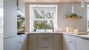 A modern kitchen with grey cabinets, a window with a view of trees, and pendant lights.