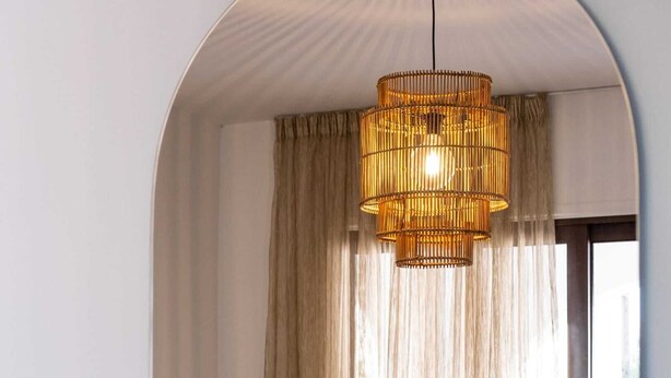 Quarto aconchegante com mesa de madeira, uma cadeira, luminária pendente e cortinas leves.