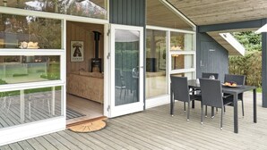 En moderne udendørs terrasse med spiseplads, pejs og en glasdør, der fører til et indre rum.