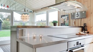 Et moderne k økken med en stålgrå bordplade, indbygget ovn og emfang. To glasstage står på bordet, og der er en potteplante i vindueskarmen.