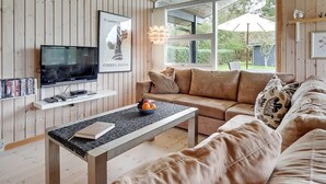 En moderne stue med TV, træpaneler, sofa og et bord med frugtskål.