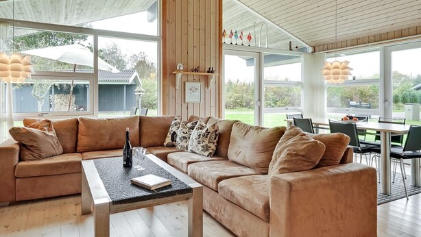 En moderne stue med en stor sofaseng, et sofabord og et spiseområde med bord og stole.