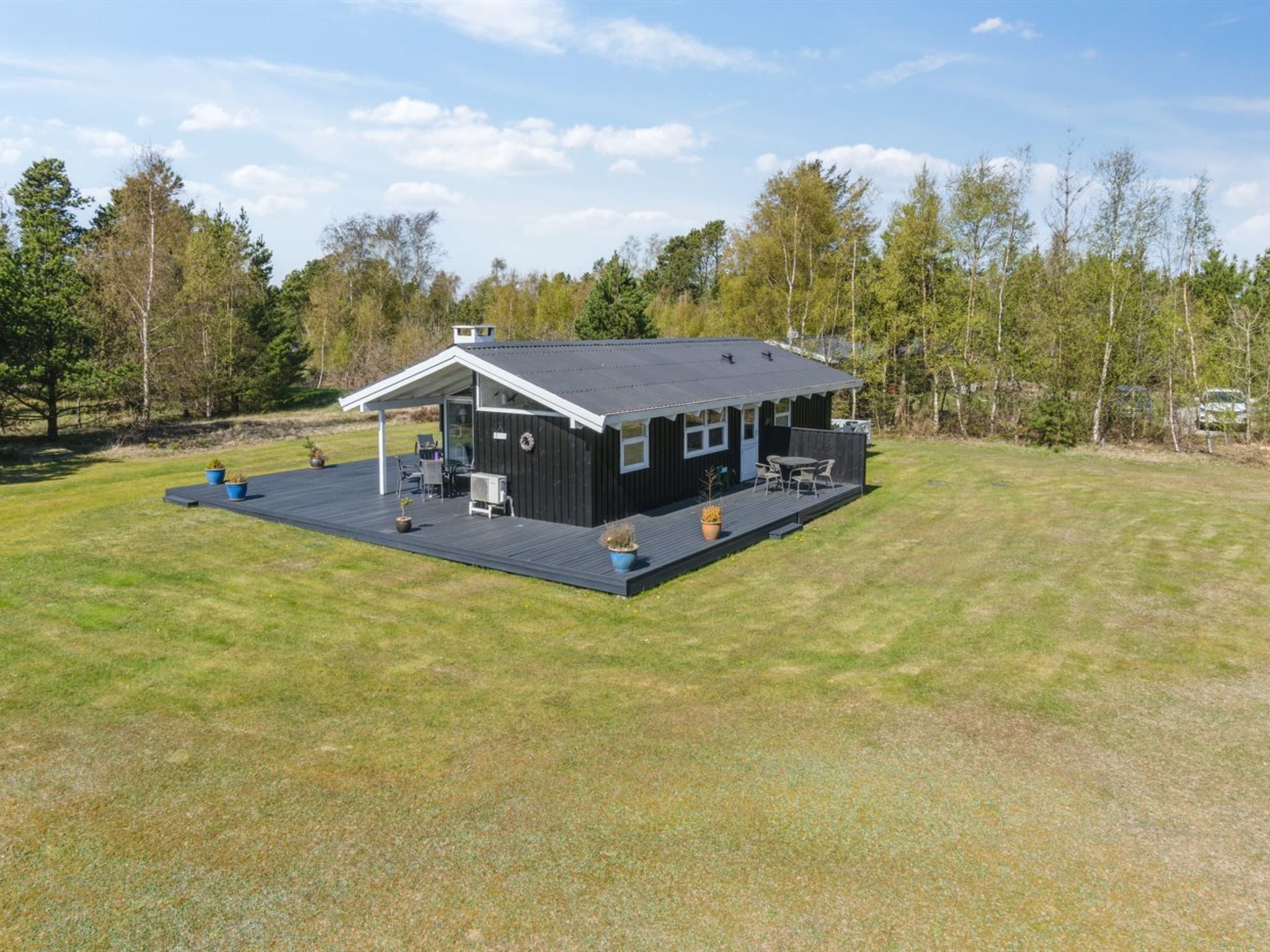 A modern black cabin with a covered patio, surrounded by a grassy field and trees.