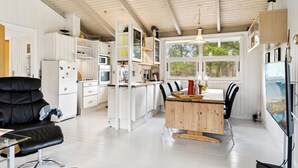 A modern kitchen with white cabinetry, a dining area with a wooden table, and a black leather chair. - "Alvine" - 475m from the sea by Interhome (Jerup)