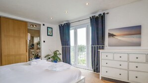 Un dormitorio con una cama grande, un tocador blanco, una ventana con cortinas y vistas a la vegetación.