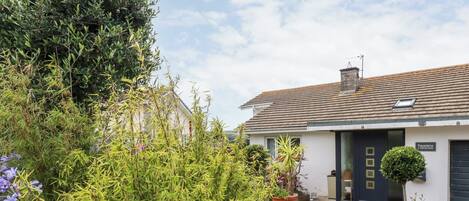 A house with a tiled roof, a front door, and a small garden with various plants and a gravel pathway.