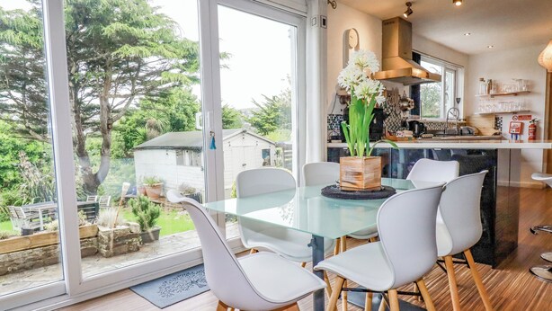 Una cocina moderna con una mesa de comedor de vidrio, sillas blancas y vistas al jardín.