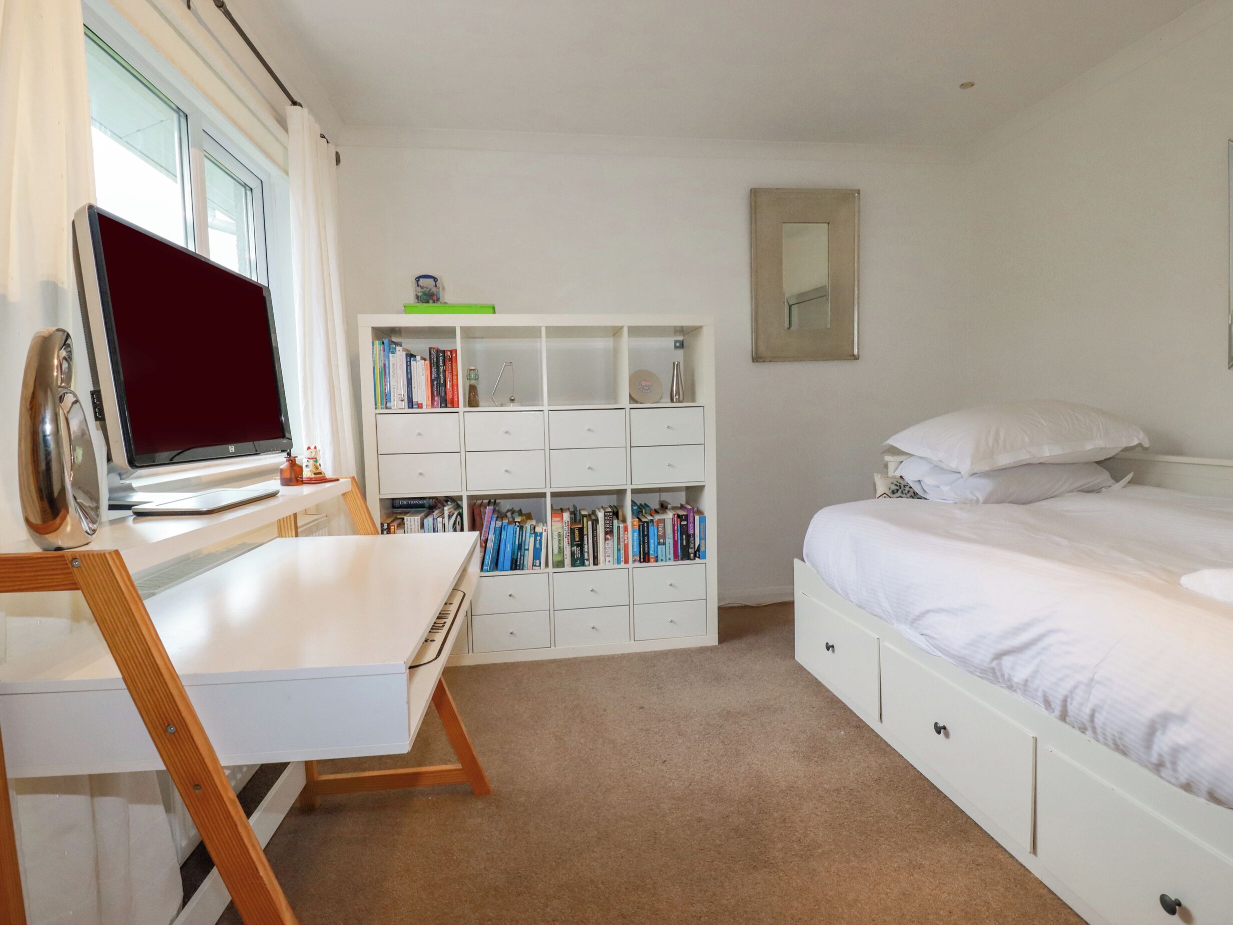 A bedroom with a bed, a desk with a laptop, a bookshelf, and a window.