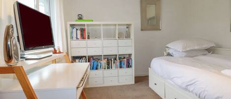 A bedroom with a bed, a desk with a laptop, a bookshelf, and a window.