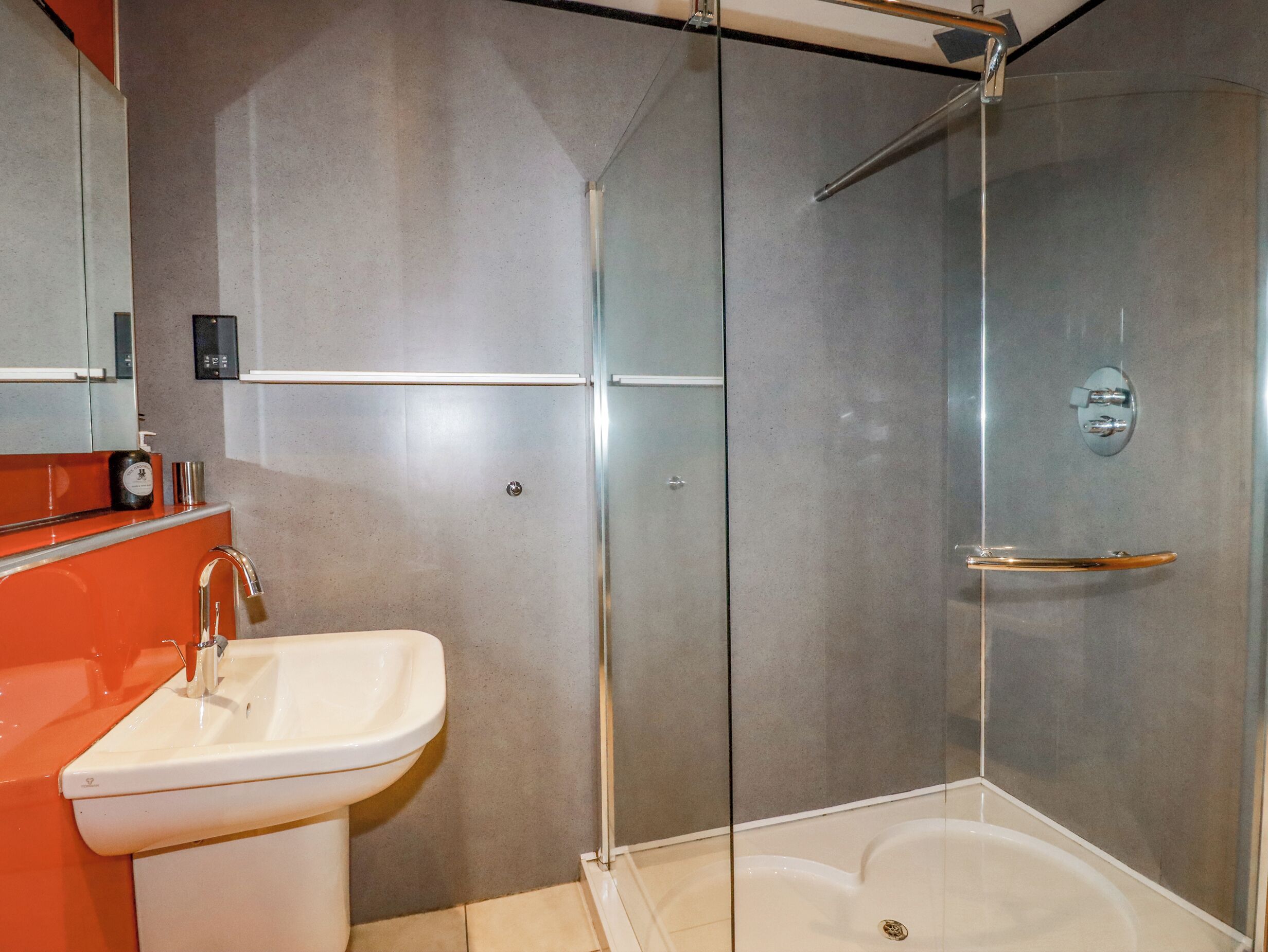 Casa de banho moderna com chuveiro de vidro, lavatório branco e espelho sobre o lavatório.