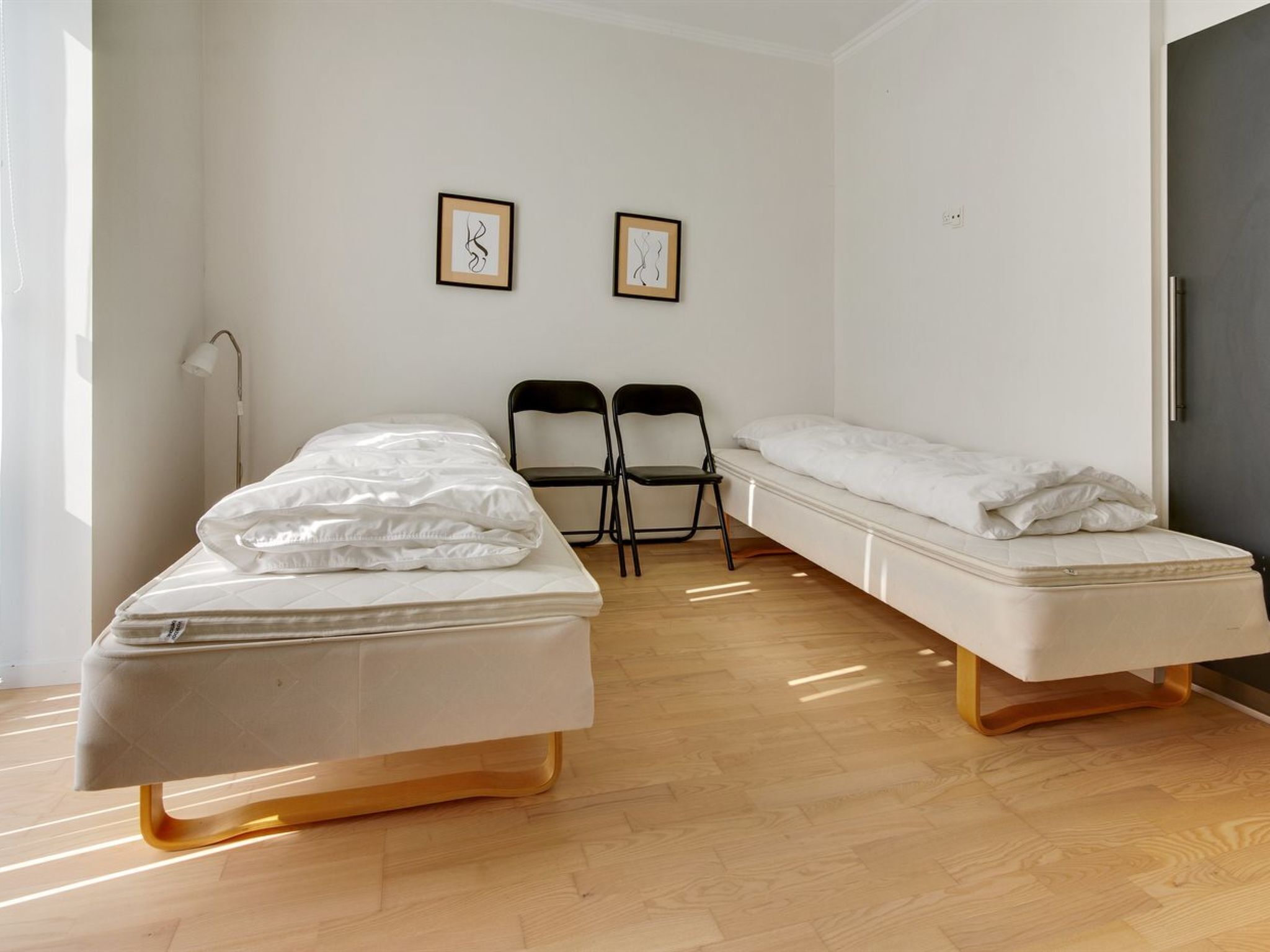 A minimalist room with two beds, a desk, and two chairs.