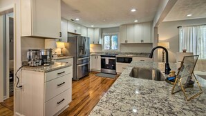 A modern kitchen with white cabinetry, stainless steel appliances, and granite countertops. - Walk to breweries, restaurants, and shops from this charming cottage featuring a private hot tub, comfortable living spaces, and easy access to Nelson 151, wineries, hiking trails, and the Blue Ridge. (Nellysford)