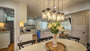 A modern kitchen with white cabinets, a dining table with a vase of flowers, and hanging light fixtures. - Walk to breweries, restaurants, and shops from this charming cottage featuring a private hot tub, comfortable living spaces, and easy access to Nelson 151, wineries, hiking trails, and the Blue Ridge. (Nellysford)