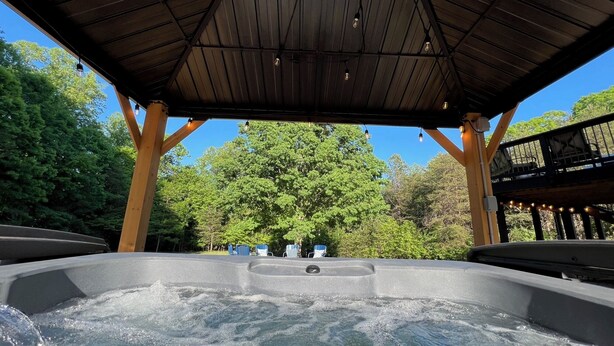 Ein Whirlpoolbereich mit einer hölzernen Pergola darüber und Blick auf Bäume im Hintergrund.