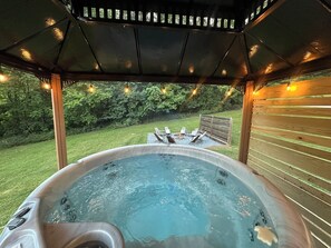A hot tub with a fire pit and lounge chairs, surrounded by a wooden deck and string lights. - Relax at a peaceful farmhouse near Nelson 151 featuring three king bedrooms, a brand-new private hot tub, fire pit, and inviting gathering spaces—just minutes from wineries, breweries, hiking, and Blue Ridge adventures. (Afton)