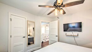 A bedroom with a bed, a ceiling fan, a TV mounted on the wall, and a door leading to a bathroom. - Relax at a peaceful farmhouse near Nelson 151 featuring three king bedrooms, a brand-new private hot tub, fire pit, and inviting gathering spaces—just minutes from wineries, breweries, hiking, and Blue Ridge adventures. (Afton)