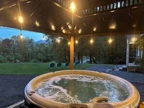 A hot tub under a covered area with string lights, surrounded by greenery and a pathway. - Gather with family and friends at Wine Cottage, a spacious 5-bedroom retreat near Nelson 151 with a covered hot tub, multiple living areas, large kitchen, game room, and plenty of space to unwind after exploring local wineries and the Blue Ridge. (Afton)