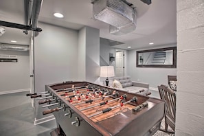 A modern room with a foosball table, a sofa, a dining table, and a staircase.