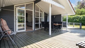 Una terraza techada con una mesa de comedor y sillas, un sofá y un sillón con una manta.