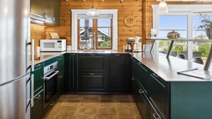 A modern kitchen with wooden beams, stainless steel appliances, and a large window overlooking greenery.