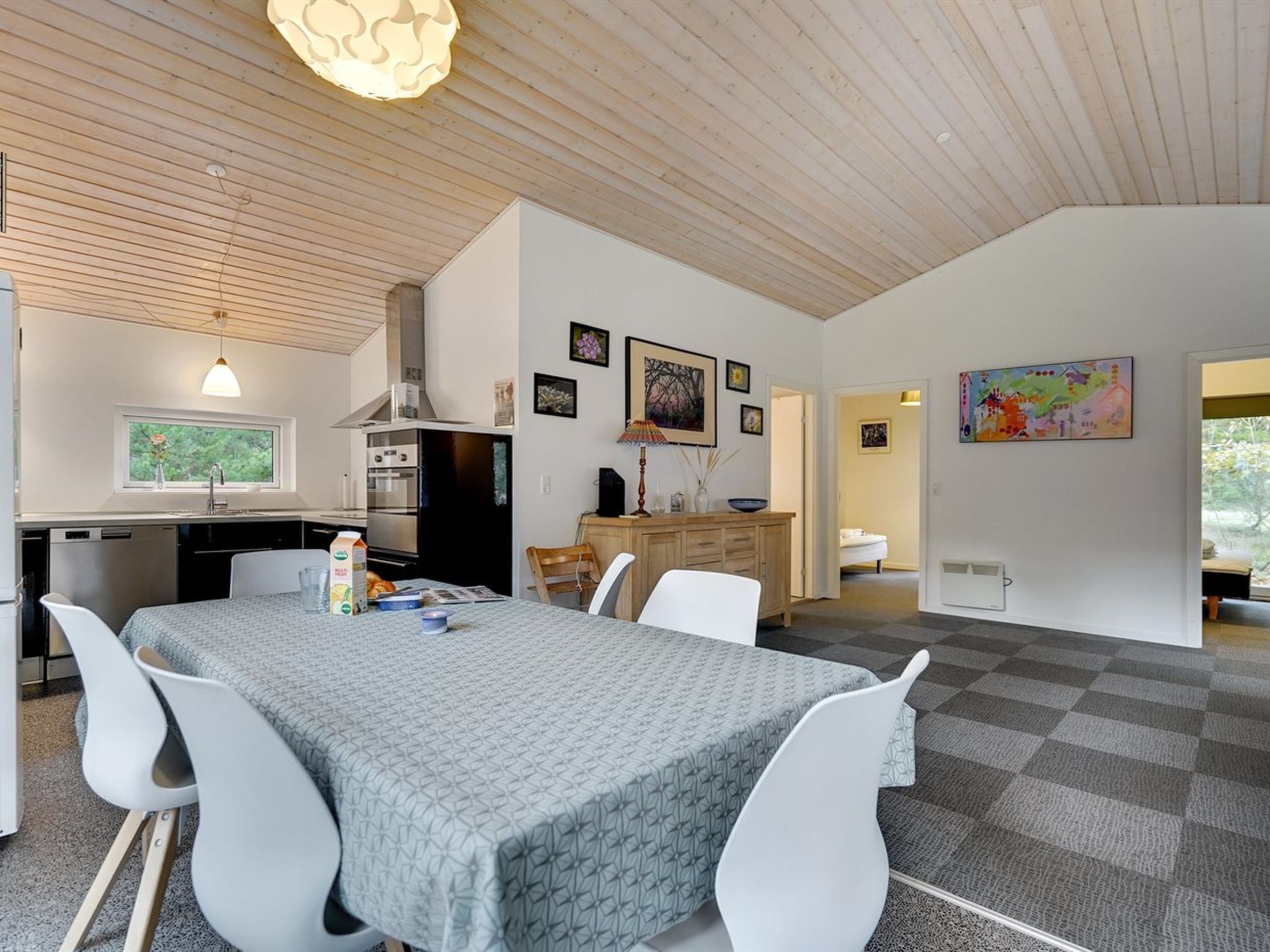 A modern kitchen with a dining area, featuring a large table, white chairs, and a view of the outdoors through a window.