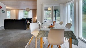 A modern dining area with a long table, white chairs, and a patterned tablecloth.