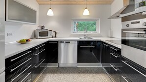 A modern kitchen with black and white cabinetry, stainless steel appliances, and a window providing a view of greenery outside.