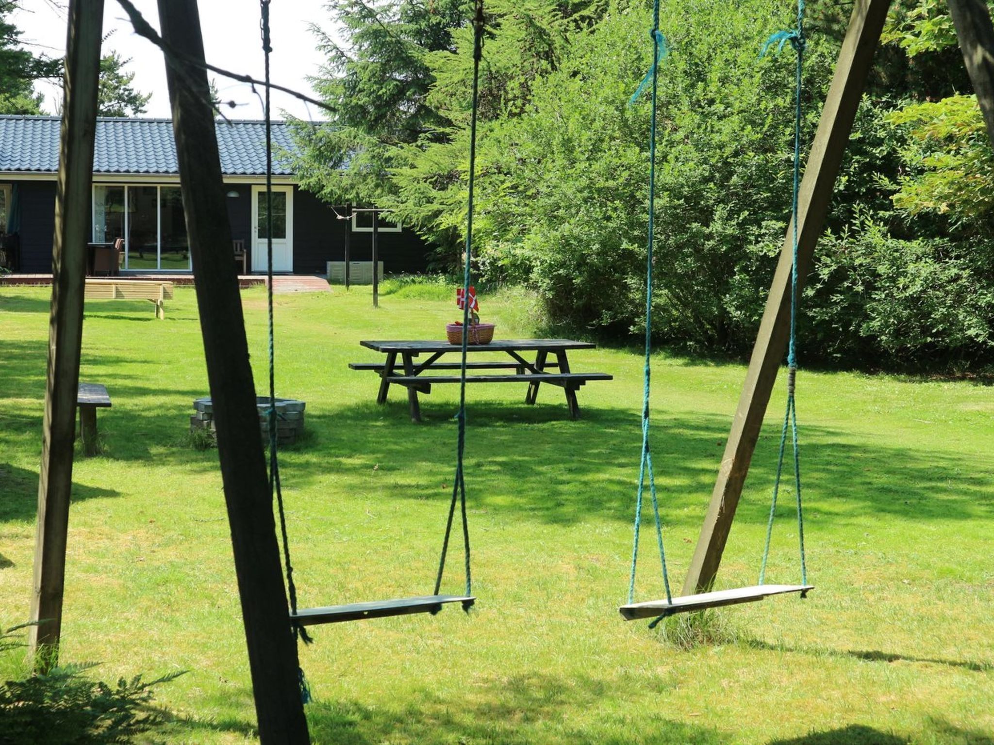 Ein grünes Außenbereich mit Schaukeln, einem Picknicktisch und einem Gebäude im Hintergrund.
